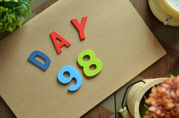 Aufkleber - Day 98, cover design in natural concept with the alphabet on brown notebook on the wooden table for a background.