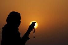 Silhouette Of A Muslim Woman Holding Prayer Beads In Her Hands And Praying At Sunset, United Arab Emirates