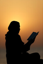 Silhouette Of A Muslim Woman Reading The Noble Quran At Sunset, United Arab Emirates