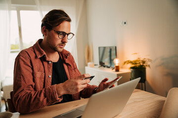 Caucasian male business man making online payment sitting at home desk holding credit card