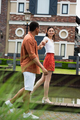 Wall Mural - cheerful asian woman holding hands with african american boyfriend while walking in city