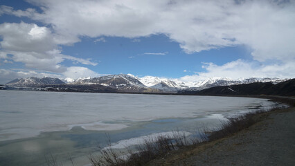 Wall Mural - Frozen lake and the coast under cloudy sky  - white hills in background