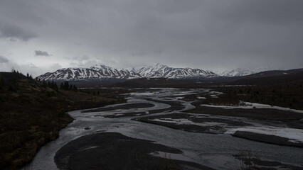 Poster - Small river streams with greenery - snowy hills in background under white sky