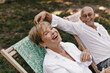 © Look! - Funny old lady with short hairstyle in white blouse, laughing and having fun with smiling husband in light shirt outdoor..