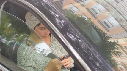 Poster - The car window closes. A woman holds phone in hand, scrolls with finger, changes hand. Glare, reflections on glass. In the background, vehicles are moving in bokeh.