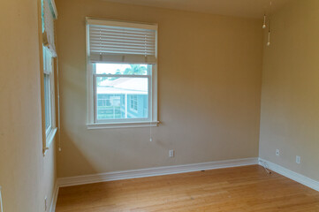 An empty neutral colored room room with wood floor and two windows