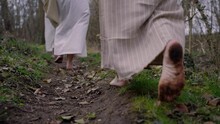Three ancient women in traditional clothing walk barefoot through the forest, backview - focus on the feets