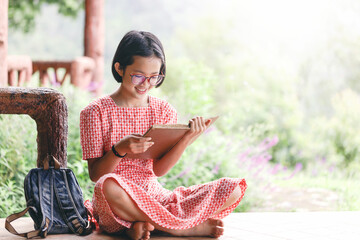 Canvas Print - Cute asian little girl with glasses reading a book in garden at summer time