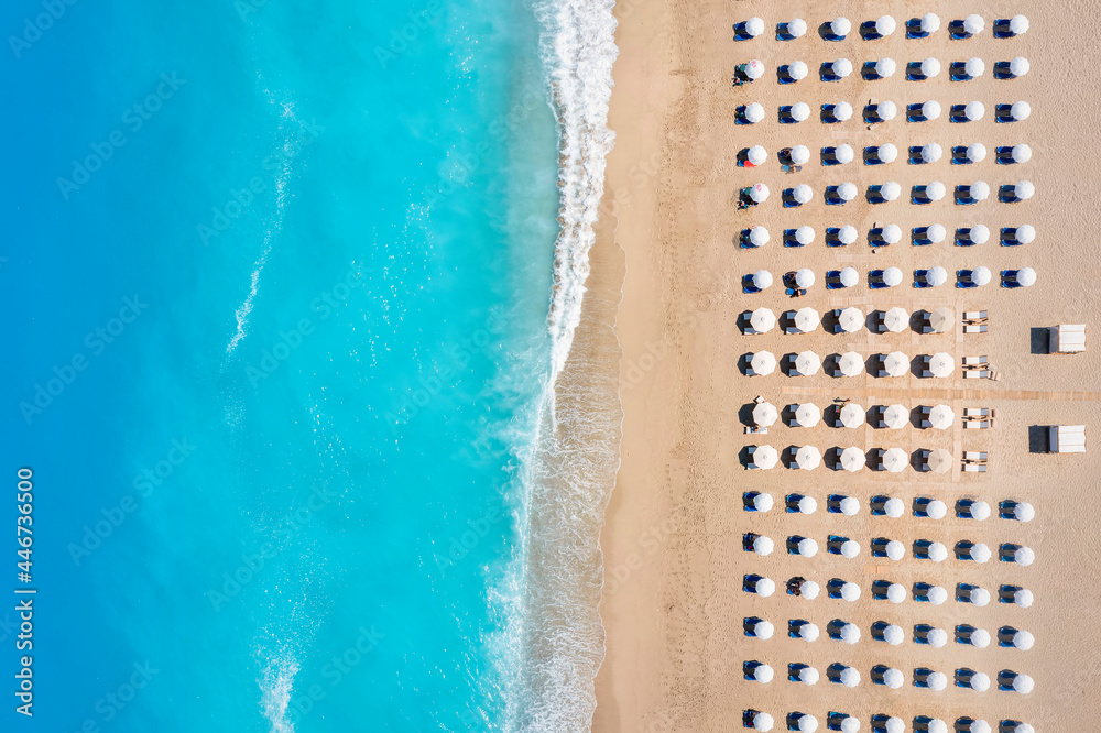 Top view of a beach with symmetrical sunbeds and parasols next to turquoise sea as seen in Greece - obrazy, fototapety, plakaty 