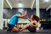 Mixed Race Friends Doing Cross Fit In The Gym. African American Male Encouraging African American Female During Sit-ups. High Quality Photo