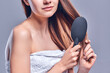 © Olena Apetroaiei - A beautiful brown-haired woman with bared shoulders looks at the camera as she brushes her hair with a brush, isolated on a gray background with copy space for text.