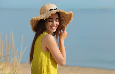 Wall Mural - Beautiful young woman wearing straw hat on beach. Stylish headdress