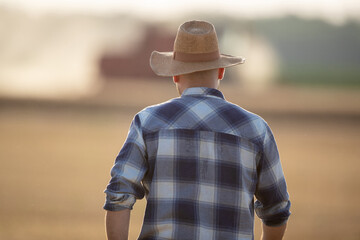 Poster - View from back of farmer walking in field. with combine harvester in background