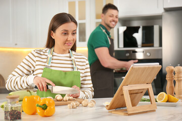 Canvas Print - Couple making dinner together while watching online cooking course via tablet in kitchen