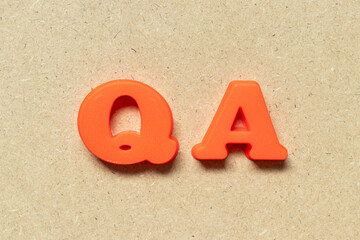 Sticker - Plastic alphabet letter in word QA (abbreviation of quality assurance or question and answer) on wood background