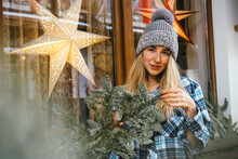 Portrait Beautiful Young Woman Decorating Outdoor House Window With Fir Tree Branches. Christmas And New Year Vibes Ideas Concept.