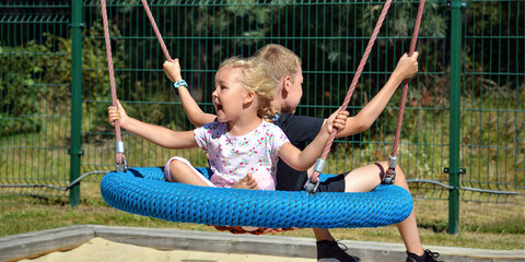 Children on a swing. Boy and girl ride a swing in the park on a summer day. Swing in the children's amusement park. banner with place for text