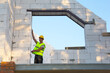 © Ольга Симонова - Construction worker at construction site measures the length of the window opening and the wall with tape measure. Cottage are made of porous concrete blocks, protective clothing - hardhat and a vest
