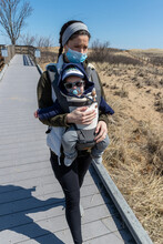 Mother Wearing Mask Walking Baby Along Beach Boardwalk.