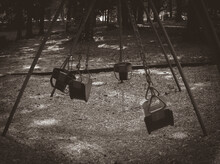 Spooky Image Of Swings Swinging With No Children. Halloween Vintage Photo Sepia Black And White Empty Seats.