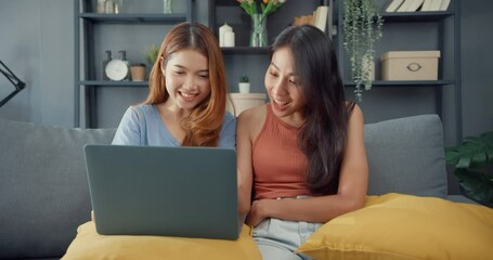 Wall Mural - Two Asia lesbian women site on couch together looking at laptop screen in living room at home together. Happy couple roommate ladies enjoy web surfing online shopping, Lifestyle woman at home concept.