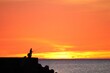 鮮やかなオレンジ色の夕焼けが美しい海と釣り人のある風景