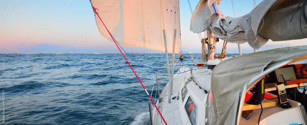 White yacht sailing in the North sea after the storm. Norway. View from the deck to the bow, mast sails. Clear blue sky, soft golden sunset light. Transportation, cruise, recreation, regatta, sport - obrazy, fototapety, plakaty 