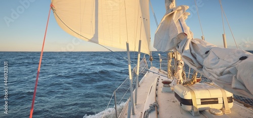 White yacht sailing in the North sea after the storm. Norway. View from the deck to the bow, mast sails. Clear blue sky, soft golden sunset light. Transportation, cruise, recreation, regatta, sport