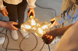 © Studio Romantic - Close up of bright light bulb in the hands of children and teachers that mean a new idea. Teacher and her younger students connect light bulbs together as a symbol of collective thinking and teamwork.