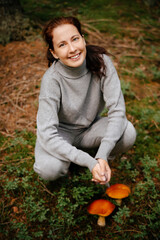 Happy woman collects edible mushrooms in the forest. Concept of hiking and harvesting.