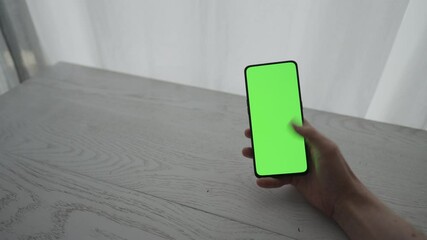 Sticker - Man showing and using smarphone with green screen while sitting behind white oak table