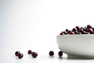 Cherries in a white cup on a white background and next to the cup scattered cherries.
