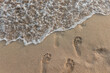 © Cavan Images - Foamy ocean water washes away footprints on sandy beach