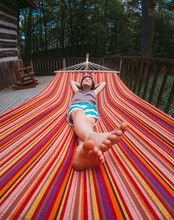 Wide Angle Of Young Boy Relaxing In A Striped Hammock On Cottage Deck.