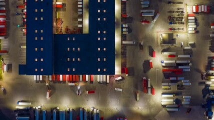 Wall Mural - Aerial top down view hyper lapse (hyperlapse - motion time lapse) of a logistics park with a loading hub. Semi-trailer trucks stand at warehouse ramps for load and unload goods at night