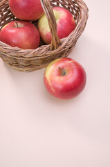 Wall Mural - Vertical shot of red apples on a wicker basket isolated on light pink background with copy space