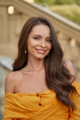 Wall Mural - Close-up face portrait of young beautiful caucasian woman with perfect natural make-up and long wavy brunette hair posing outdoors at sunset