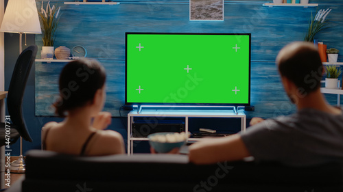 Caucasian people watching green screen layout on tv display in living room at home. Young man and woman looking at copy space and chroma key for isolated template and mockup background