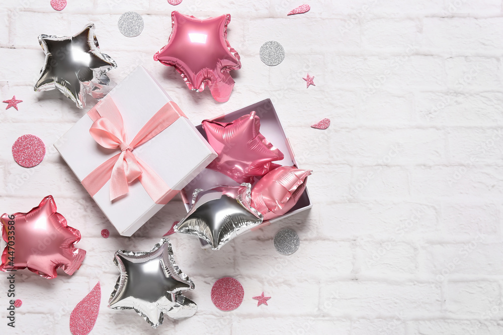 Gift box with festive air balloons on light brick background