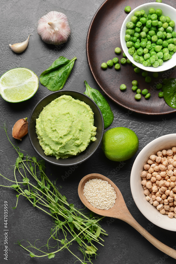 Composition with tasty green pea hummus, lime and chickpeas on dark background