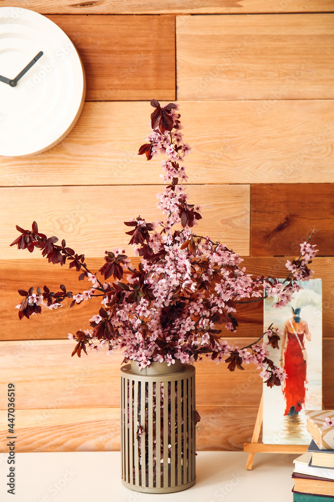 Vase with blooming branches and picture on table against wooden background