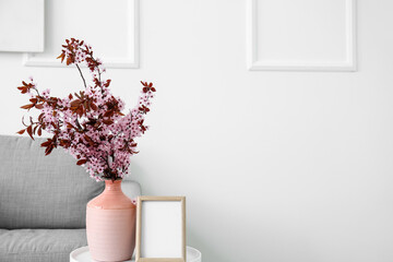 Wall Mural - Vase with blossoming branches and blank frame on table near light wall