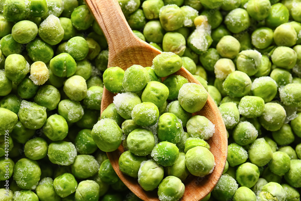 Spoon with frozen green peas as background
