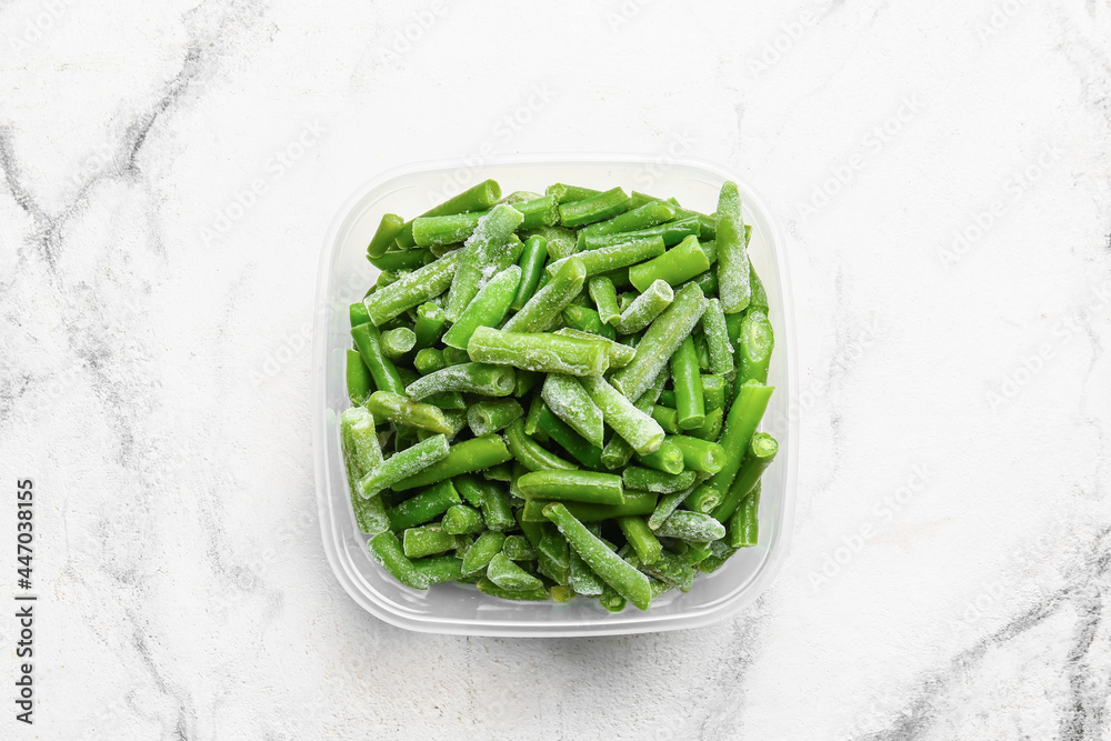 Container with frozen green beans on light background
