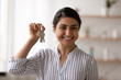 Head shot portrait of smiling Indian woman showing keys, looking at camera, happy young female tenant renter satisfied buyer client excited by relocation, proud homeowner purchasing new apartment