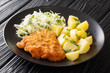 Fried pork cutlet breaded served with potatoes and cabbage salad close-up in a plate on a black wooden background. horizontal
