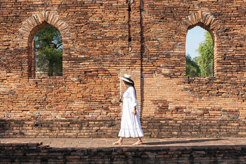 A female traveler walks through a wall of ruins archaeological sites in Wat Phra Si Sanphet, Ayutthaya