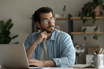 thoughtful young business man in glasses sit at desk distracted from computer work looks into distan