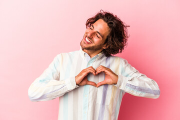 Young caucasian man isolated on pink bakcground smiling and showing a heart shape with hands.