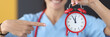 © H_Ko - Smiling nurse points finger at red alarm clock